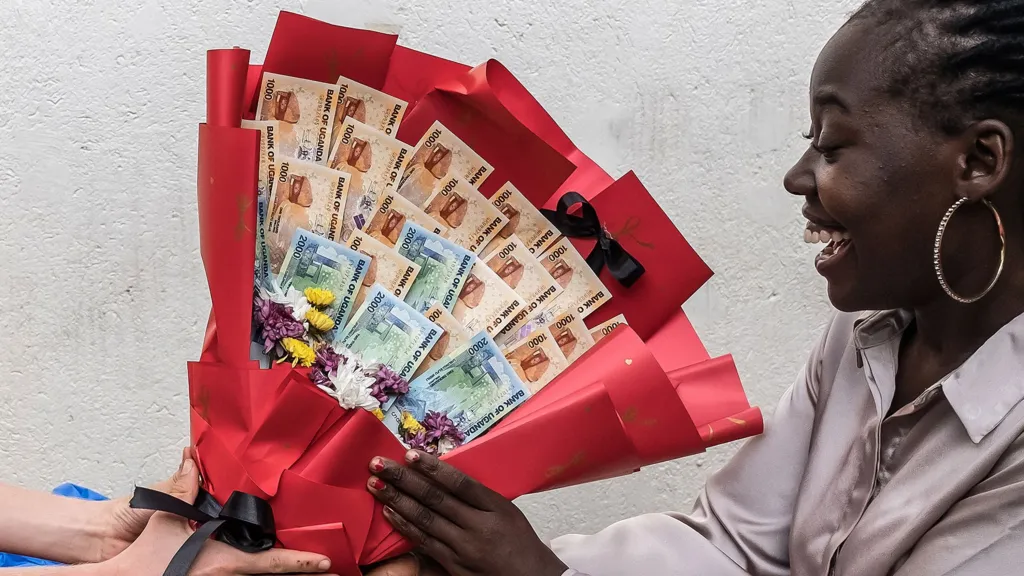 A woman smiles as she receives a bouquet made of banknotes and flowers from her boyfriend as a surprise ahead of Valentine's Day during a hangout in Kampala on February 7, 2026.