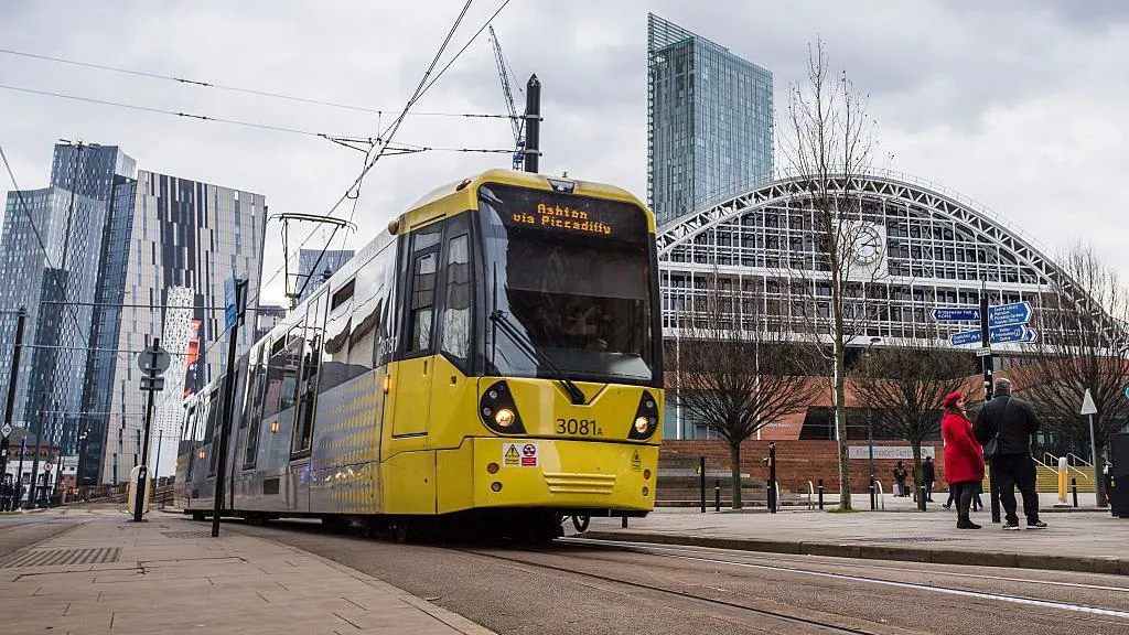 A yellow Manchester tram driving past with some modern skyscrapers in the background