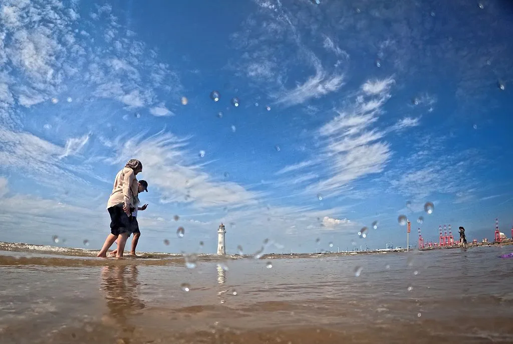 new brighton beach in bright sunshine. Two people are paddling in the shallows,