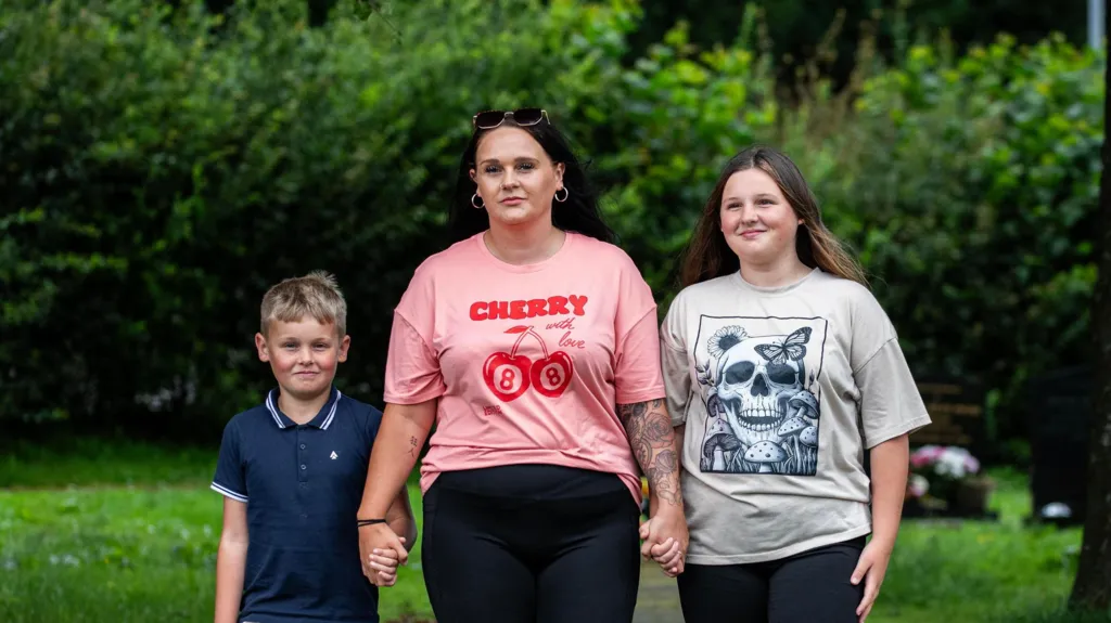 Photograph of Hazel Jones (centre) pictured with her daughter Amelia, 13, (right) and her son (left). Hazel Jones wears a pink t-shirt with red writing on the front which reads "cherry". Her daughter wears a grey t-shirt with a navy skull design, while her son wears a navy polo shirt and has short blonde hair.