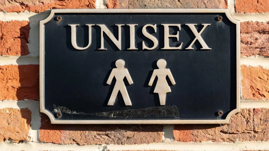 A sign that reads "unisex" on a brick wall in an unknown location.