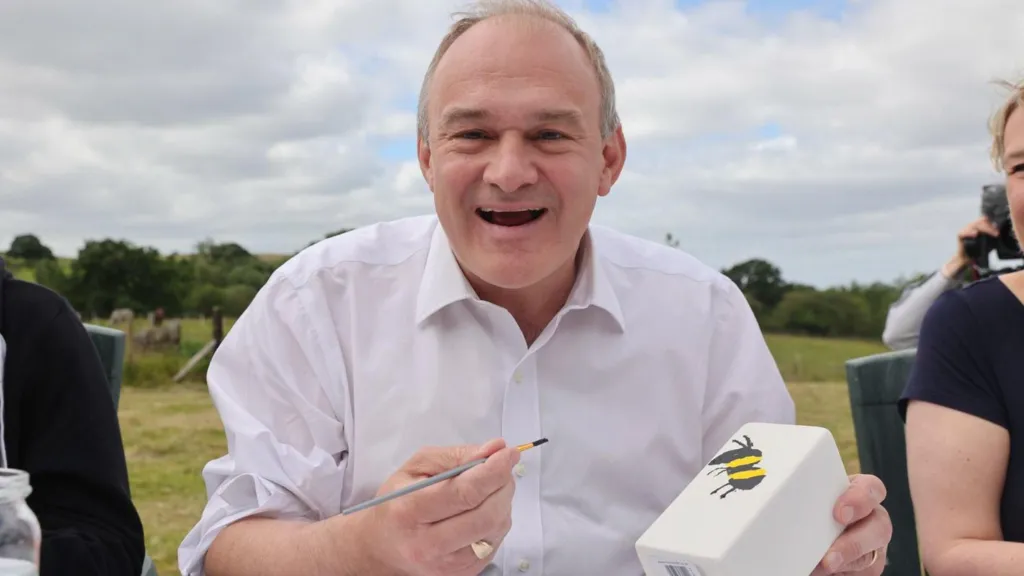 Liberal Democrat leader Sir Ed Davey holding a paintbrush in the one hand and in the other a pot with a bee painted on the side.