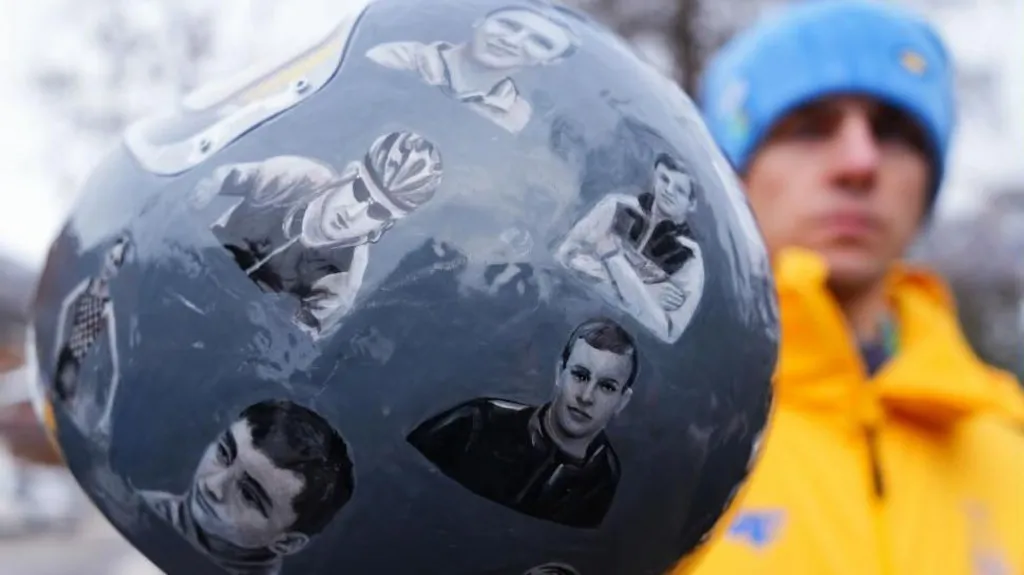 A close up shot of the "helmet of remembrance" worn by Ukrainian athlete Vladyslav Heraskevych. The grey helmet features athletes killed in the war in Ukraine since Russia's full-scale invasion. A blurred Heraskevych holding the helmet is pictured in the background.