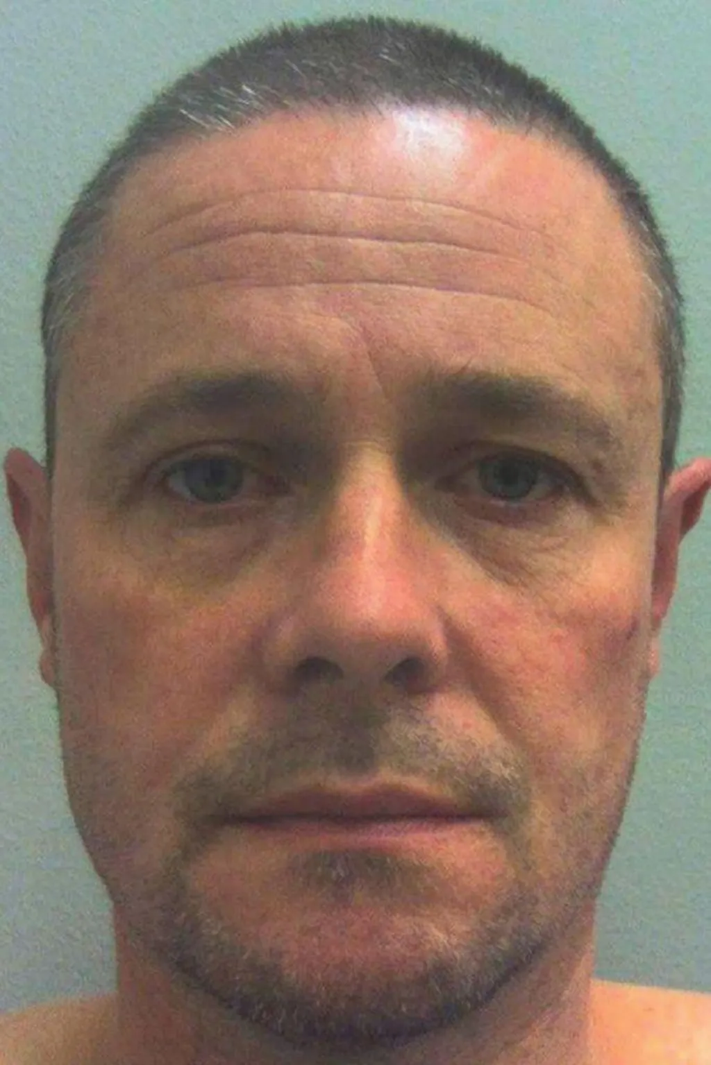 Mugshot photograph of Mark Bridger, aged 47 at the time, who has blue eyes and short grey hair. A white wall with a blue hue can be seen in the background.