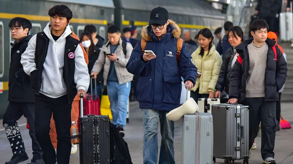 Young travelers pull their suitcases and check their phones while walking along the platform of Fuyang Railway Station. 