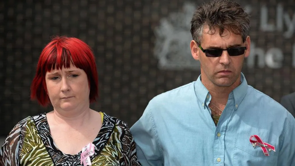 Photograph of Paul Jones (right) in 2013. He wears a blue shirt with a pink breast cancer bow on his shirt pocket.His wife and April's mum, Coral (left), has bright red and black hair in a bob. She wears a black and white zebra blouse.