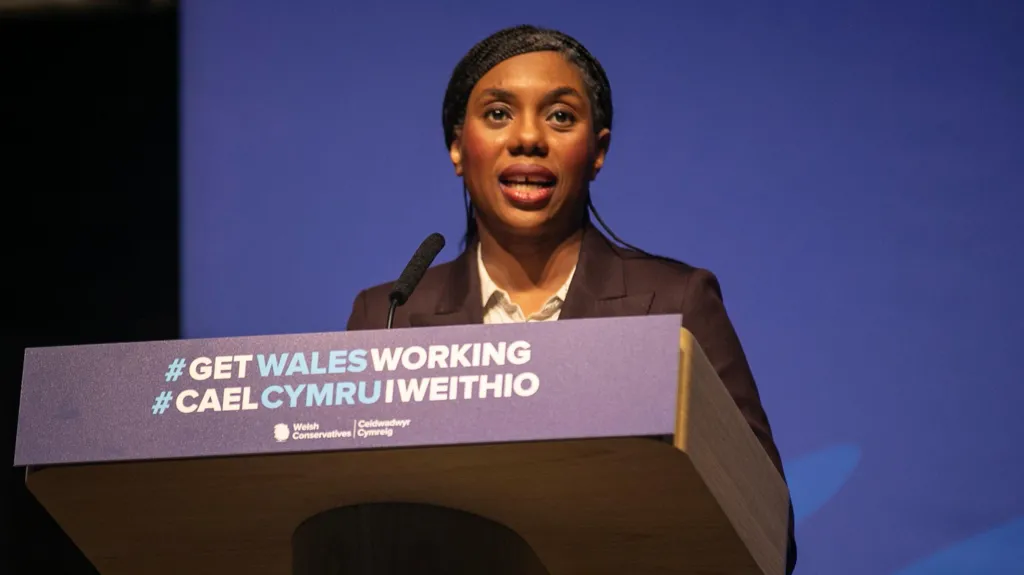 Kemi Badenoch stood at a lectern that reads "#Get Wales Working" in Welsh and English.